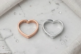 Comparatif de deux bagues cœur magnétiques BFF en or rose brossé et argent poli posées sur marbre blanc